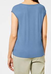 Sininen lyhythihainen paita pyöreällä pääntiellä ja pehmeää kangasta. Tasainen rakenne rentoa istuvuutta, yhdistettynä vaaleisiin housuihin.