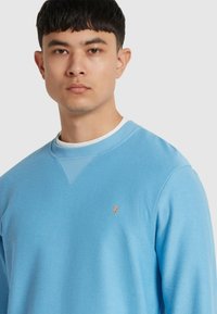 Morbido maglione azzurro con una finitura testurizzata, dotato di scollo rotondo e di un piccolo logo ricamato sul petto.