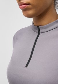 Top lavanda aderente con colletto alto, zip nera corta e tessuto testurizzato. Presenta maniche raglan e una superficie liscia.