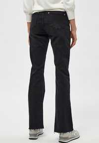 Jeans acampanados negros con cinturilla de altura media, dobladillo deshilachado y dos bolsillos traseros. Hechos de denim con una textura suave, combinados con calzado claro.