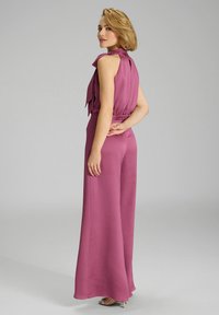Getailleerde mouwloze jumpsuit in mauve, met een hoge neklijn en wijde broekspijpen. Soepele textuur met een strikaccent op de rug.