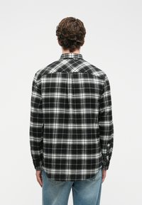 Camisa de flanela às rimadas em preto e branco, de mangas longas, com design de botões, bainha arredondada, feita de tecido macio com acabamento texturizado.