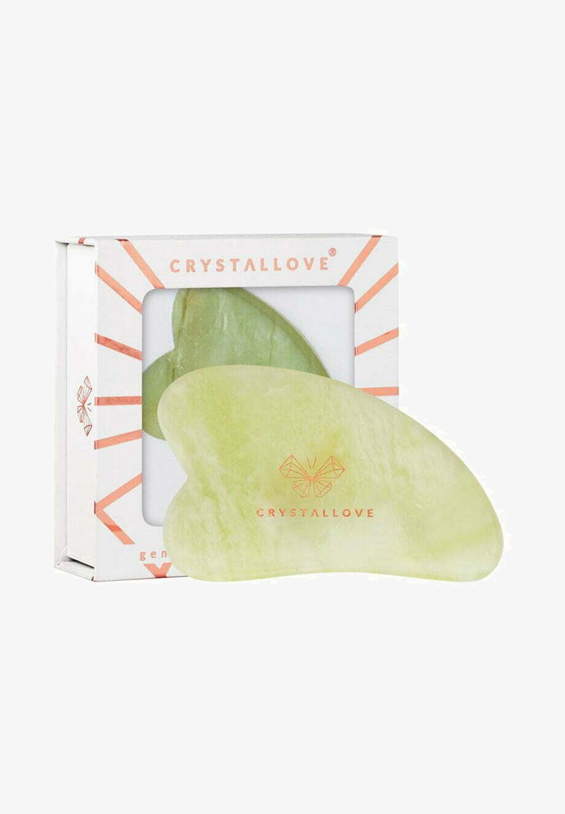 Strumento gua sha verde a forma di cuore con una superficie liscia e lucidata. Imballato in una scatola con uno sfondo bianco e accenti geometrici.