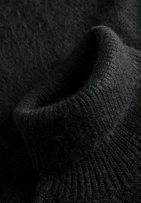 Maglione nero lavorato a maglia con un colletto alto e testurizzato, dalla finitura leggermente pelosa e con polsini a costine, sottolineando calore e comfort.