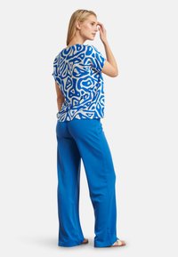 Kortekleurige top met blauwe en witte patronen en een afgeronde zoom, gecombineerd met effen blauwe wijde broek; zachte stof; relaxte pasvorm.