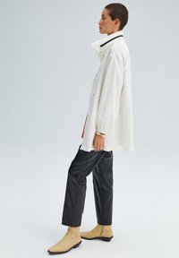 Giacca bianca oversize con colletto alto, accento nero, abbinata a pantaloni neri simili alla pelle e stivaletti beige alla caviglia. Tessuto liscio, vestibilità comoda.