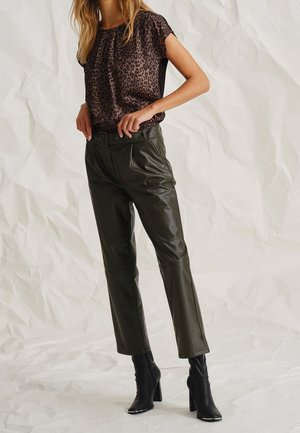 Blouse à imprimé léopard noir et marron avec un col froncé, associée à un pantalon en faux cuir olive avec une taille ceinturée et une coupe ajustée.