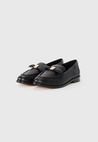 Black loafers made of textured leather, featuring a bow accent with a gold hardware piece, low heel, and stitched detailing along the edge.