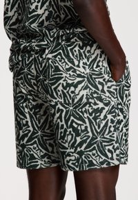 Grüne und weiße gemusterte Shorts aus strukturiertem Stoff, mit einem blütenähnlichen Design und seitlichen Taschen.