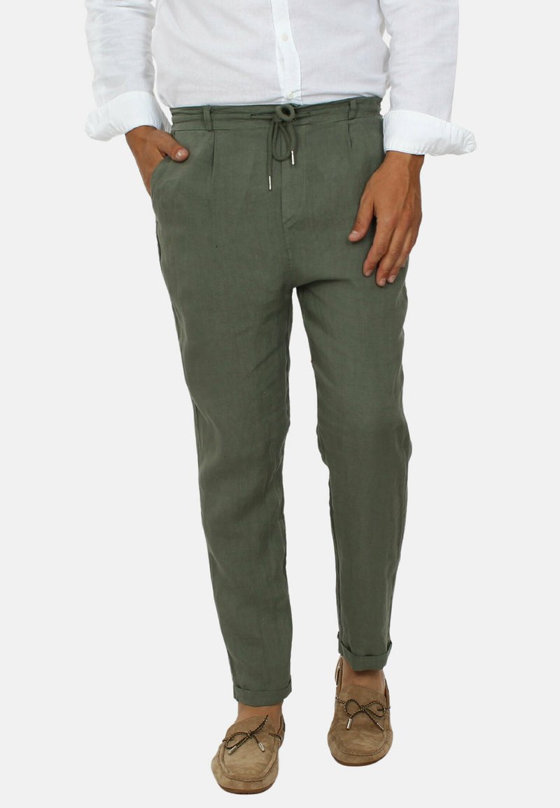 Pantaloni di lino verde oliva con vita regolabile, taglio tapered e orli risvoltati; abbinati a mocassini marrone chiaro e una camicia bianca.
