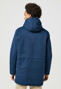 Chaqueta aislante azul marino con capucha, que presenta una textura suave, detalles de costura y un diseño de longitud media.