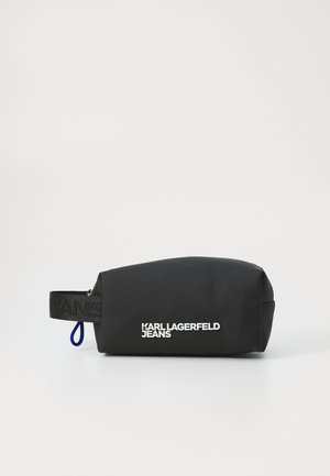 Black cosmetic pouch with a rounded shape, made from smooth material. Features a textured black strap with embossed "JEANS" and white logo print.
