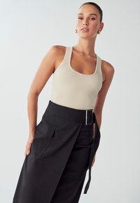 Ribana bež majica na naramenice širokega kroja, kombinirana z visokimi črnimi hlačami, ki imajo stranski žep in širok pas.