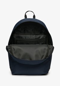 Sac à dos bleu marine de forme arrondie, doté d'une fermeture éclair. L'intérieur est noir avec des poches organisatrices et un compartiment en maille.
