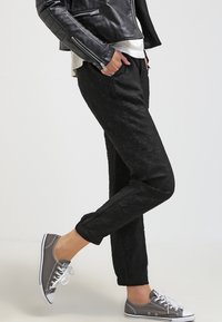 Zwarte broek met een gestructureerd bloemenpatroon, taps toelopende fit en elastische boorden, gecombineerd met grijze sneakers en een zwart leren jack.
