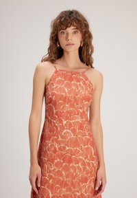 Rot-orange Kleid mit einem blattähnlichen Muster, dünnen Trägern und einem eng anliegenden Oberteil, aus einem leichten Stoff.