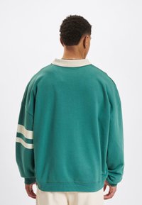Sweatshirt teal cu guler alb, având trei dungi albe pe mâneci și o croială lejeră. Material moale cu manșete ribbate.