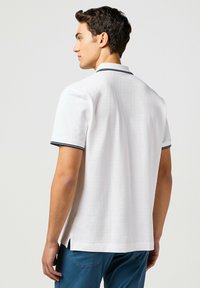 Weißes Kurzarm-Poloshirt mit navygestreiftem Kragen, gerade geschnitten mit Seitenschlitzen. Hergestellt aus glattem Baumwollstoff.