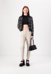 Čierno-biely károvaný saká, priliehavý čierny crop top, béžové zúžené nohavice, čierne platformové topánky a malá čierna taška.