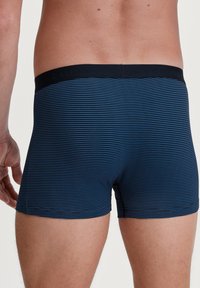 Pantaloni boxer blu navy con righe orizzontali in blu chiaro. Vita elastica con il nome del marchio "CALIDA" impresso. Tessuto morbido.