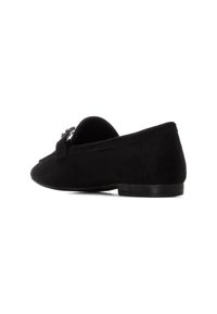 Zapato de gamuza negra con un tacón bajo, punta redondeada y un acento decorativo de hardware plateado. Textura suave, diseño sencillo y silueta elegante.