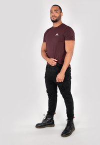 Bordeauxrotes T-Shirt mit kurzen Ärmeln und Logo, kombiniert mit schwarzen Cargo-Hosen mit Taschen und schwarzen Schnürstiefeln. Einfaches, figurbetontes Design.