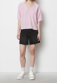 Top V della lunghezza delle maniche corta, in rosa chiaro, con scollo a V, abbinato a pantaloni corti in denim scuro. Look completato con sneakers bianche e calze grigie a coste.