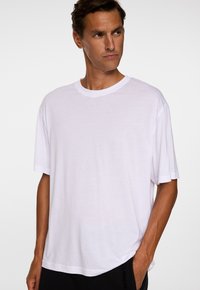 Vit kortärmad t-shirt med rund halsringning, med en slät yta och en avslappnad passform. Subtil sömnadsdetalj vid fållen.