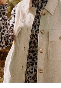 Cremfarbener Wollmischungsweste mit großen Knopfverschlüssen und zwei vorderen Taschen, übereinander getragen mit einem schwarz-grauen Leopardenmuster-Oberteil mit elastischen Bündchen.