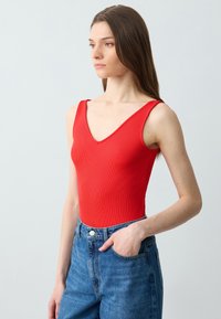 Body rosso a coste con scollatura a V profonda, abbinato a jeans in denim blu a vita alta. Texture liscia e silhouette aderente.