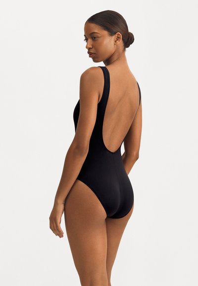 Melnas viengabala peldkostīms ar zemu aizmuguri, plašiem siksnām un gludu, elastīgu audumu. Vienkāršs dizains, bez rakstiem vai akcentiem.