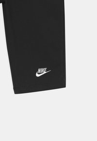 Pantalones cortos deportivos negros hechos de tela elástica, con costuras planas y un logotipo de Nike bordado en blanco en la parte inferior de la pierna izquierda.