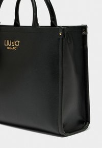 Sort læder tote taske med tekstureret finish, gulds logo detaljer, robuste håndtag og en sikker lynlås; rektangulær form.