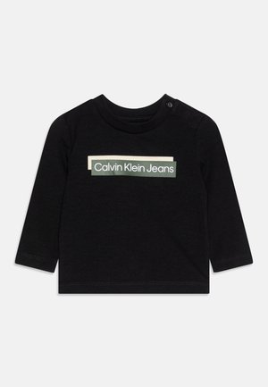 Schwarzes Langarmshirt aus Baumwolle mit Rundhalsausschnitt. Auf der Vorderseite befindet sich ein weißes und grünes "Calvin Klein Jeans"-Logo. Knopfdetail an der Schulter.
