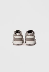 Nike sportbačiai iš pilkos zomšos su baltomis detalėmis, turintys paminkštintą apykaklę, tekstūruotus šoninius paviršius ir gumos padą su raštu.