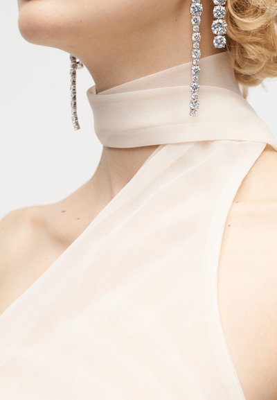 Close-up of a person wearing a sheer, pale halter neck top with a matching neck wrap and long dangling rhinestone earrings.