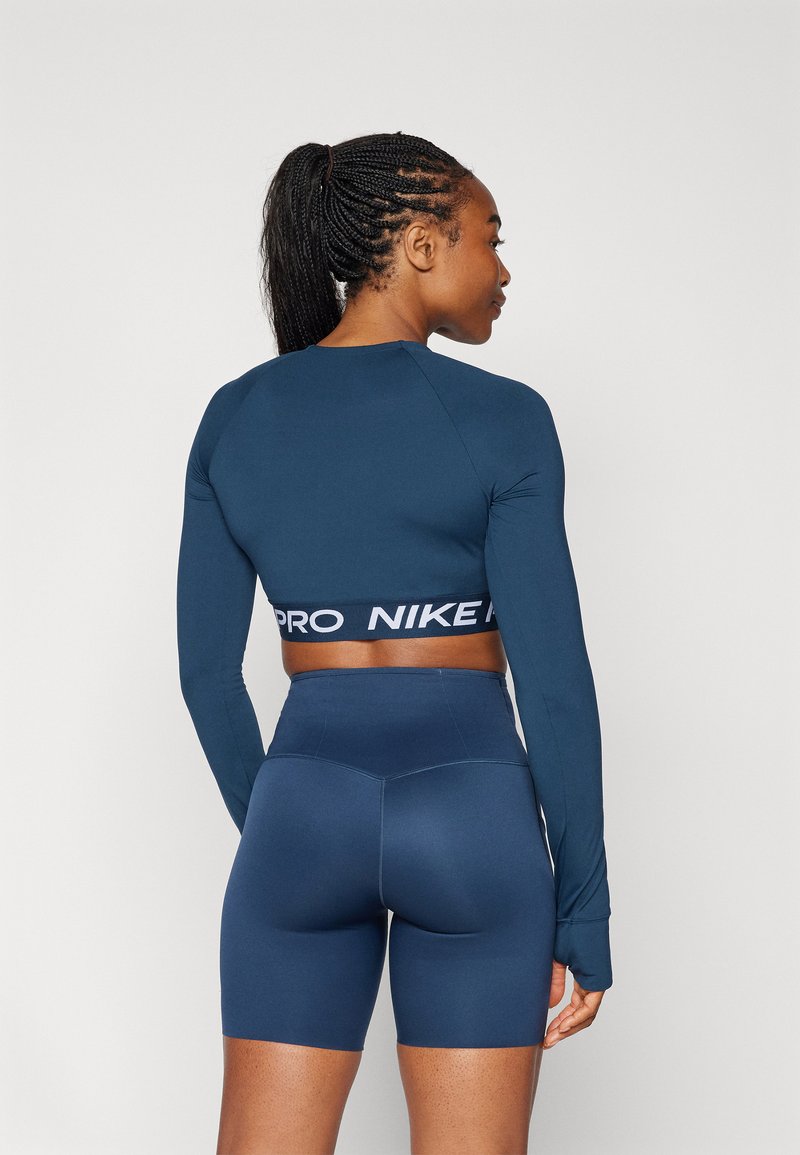Marineblaue Langarm-Crop-Top mit weißem "PRO NIKE" Branding, kombiniert mit passenden hochtaillierten Shorts. Glatte, dehnbare Stoffe.