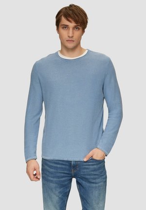 Blue long-sleeve shirt in soft fabric with a crew neckline and a slight heather pattern. Paired with blue denim jeans.