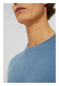 Sudadera azul claro con cuello redondo, que presenta una textura suave y detalles de costura inclinada en los hombros. Diseño simple y minimalista.