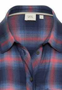 Plaid shirt featuring a dark navy base with red and blue accents, short collar, and button-down front. Made of woven fabric with texture.