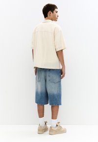 Beige short-sleeve shirt with a textured finish, paired with light blue denim shorts that fade to darker blue at the hem. Sneakers and white socks.