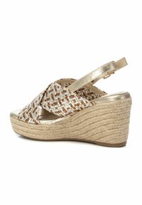 Sandalia de cuña con parte superior de tela trenzada en dorado y marrón, correa ajustable en el tobillo y suela de cuerda natural texturizada.