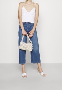 Valkoinen lyhyt toppi, jossa on spagettiolkaimet, siniset leveälahkeiset farkut ja kermavärinen tilkkupussikassi, jossa on ryppyosat. Valkoiset hihnakengät.