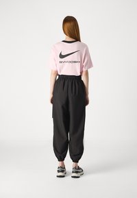 Rosa t-skjorta med korta ärmar och svart krage, i kombination med svarta joggingbyxor med elastisk midja och neutrala sneakers.