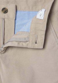 Pantalons beiges avec une doublure bleue, dotés d'une fermeture éclair et d'une fermeture à bouton. Le tissu a une texture lisse, avec des coutures détaillées.