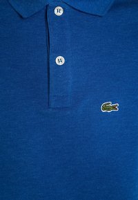 Modrá polo košile z texturované tkaniny s klasickým límcem, tříknoflíkovou légu a malým vyšívaným zeleným krokodýlem logo.