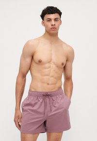 Purple swim shorts made of lightweight material, featuring an elastic waistband with a drawstring and side pockets.
