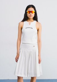 Hvit ribbet tanktopp med "DICKIES" logo, kombinert med en plisserte hvite nederdel. Modellen har på seg refleksible oransje solbriller. Glatt tekstur.