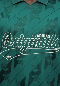 Πράσινο μπλουζάκι Adidas Originals με γεωμετρικό σχέδιο και μεγάλο λευκό κείμενο "Originals" στο στήθος.