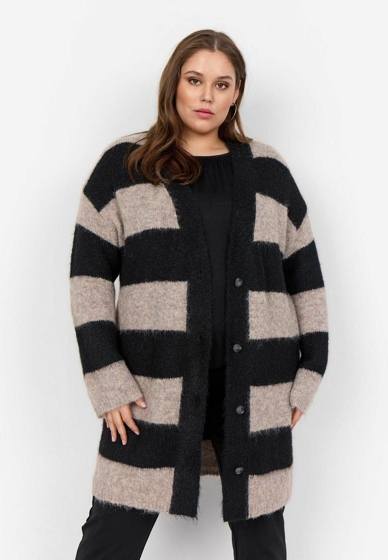 Cardigan surdimensionné en tricot doux et texturé. Présente de grandes rayures noires et beiges, des boutons sur le devant et une coupe décontractée, idéale pour le superposition.